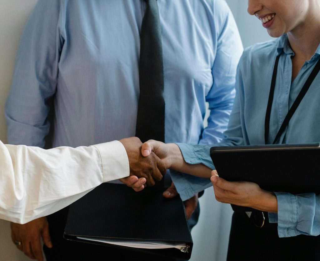 Crop unrecognizable diverse partners in formal clothes with documents shaking hands during business meeting in office